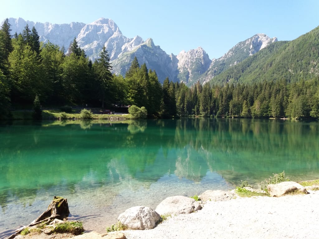 Lago alpino con acque cristalline, boschi e montagne sullo sfondo